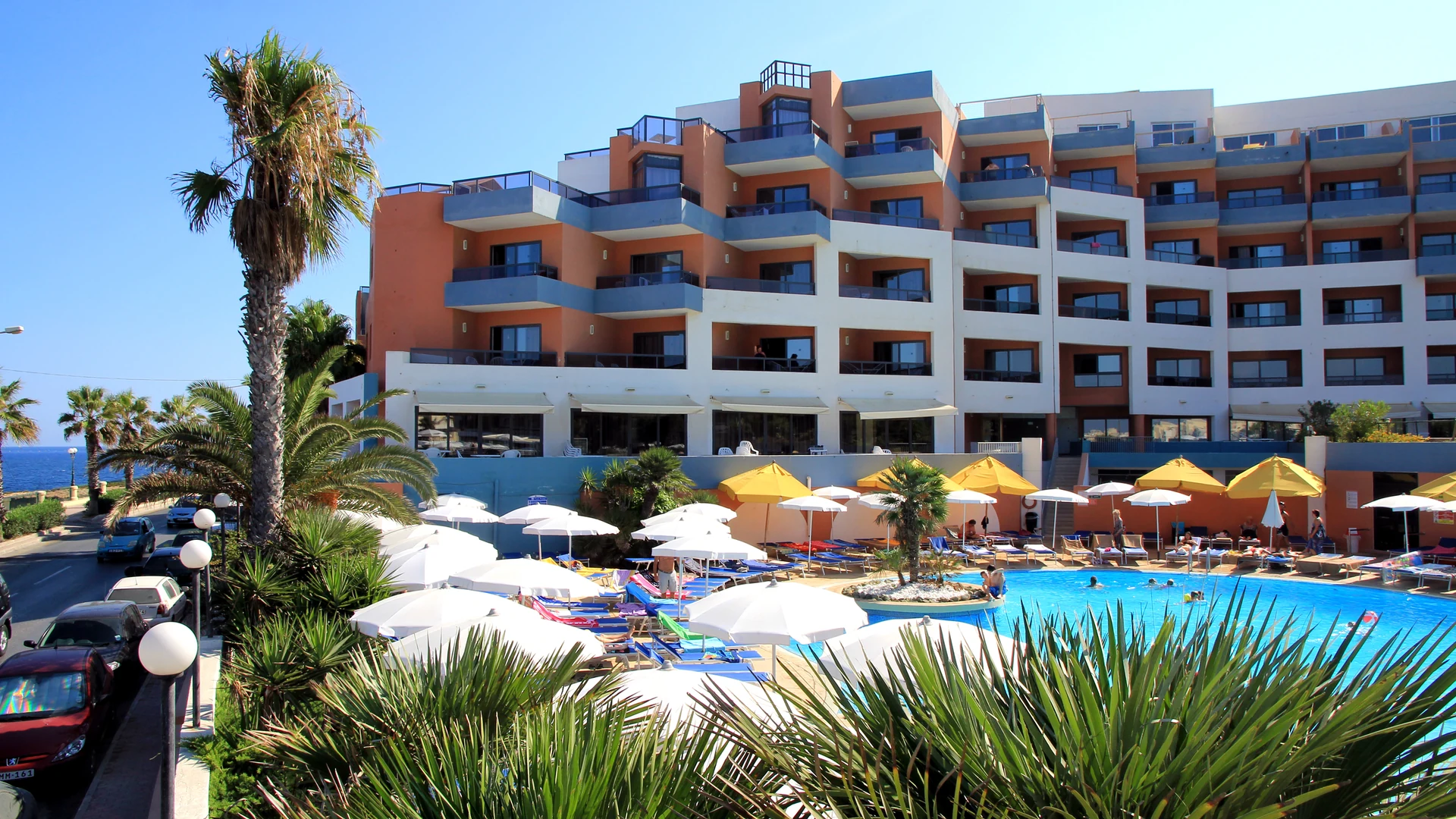 An all-inclusive resort in Malta with an outdoor pool, sun loungers and parasols below the hotel