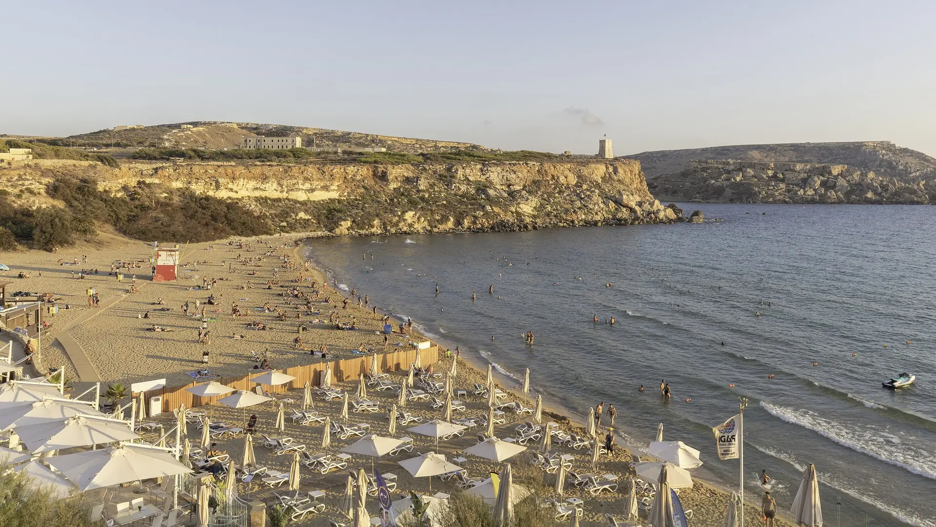 Golden sandy bay with clear turquoise water and low cliffs on the north coast of Malta
