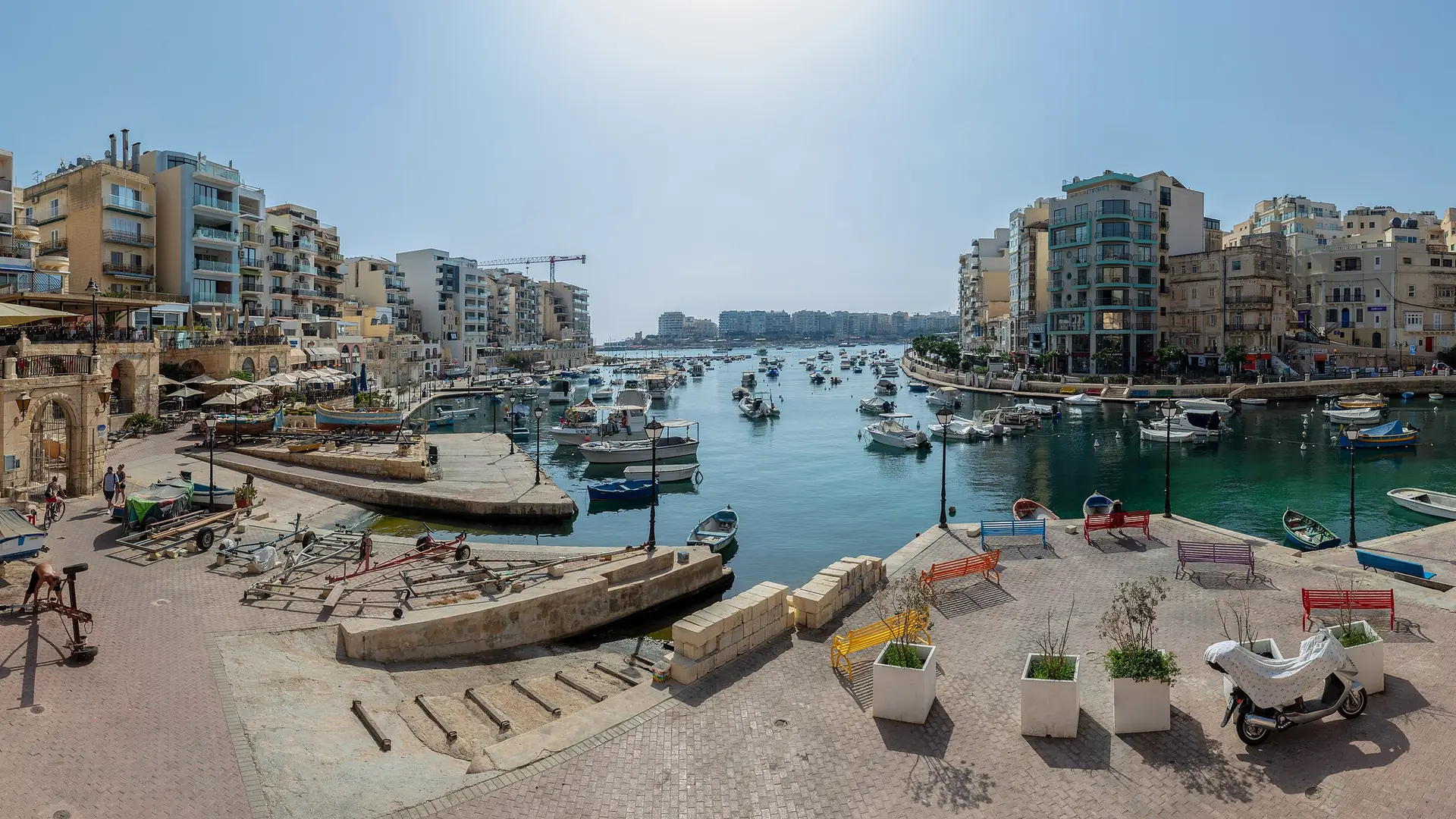 Sunny waterfront with traditional boats at Spinola Bay, St Julian's, Malta under a clear sky