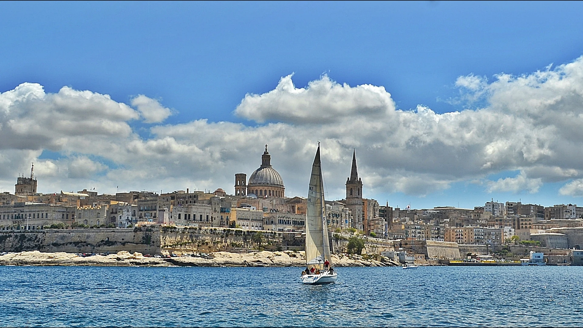 Valletta's skyline rising above the bastions across Marsamxett Harbour, with a yacht passing in the foreground