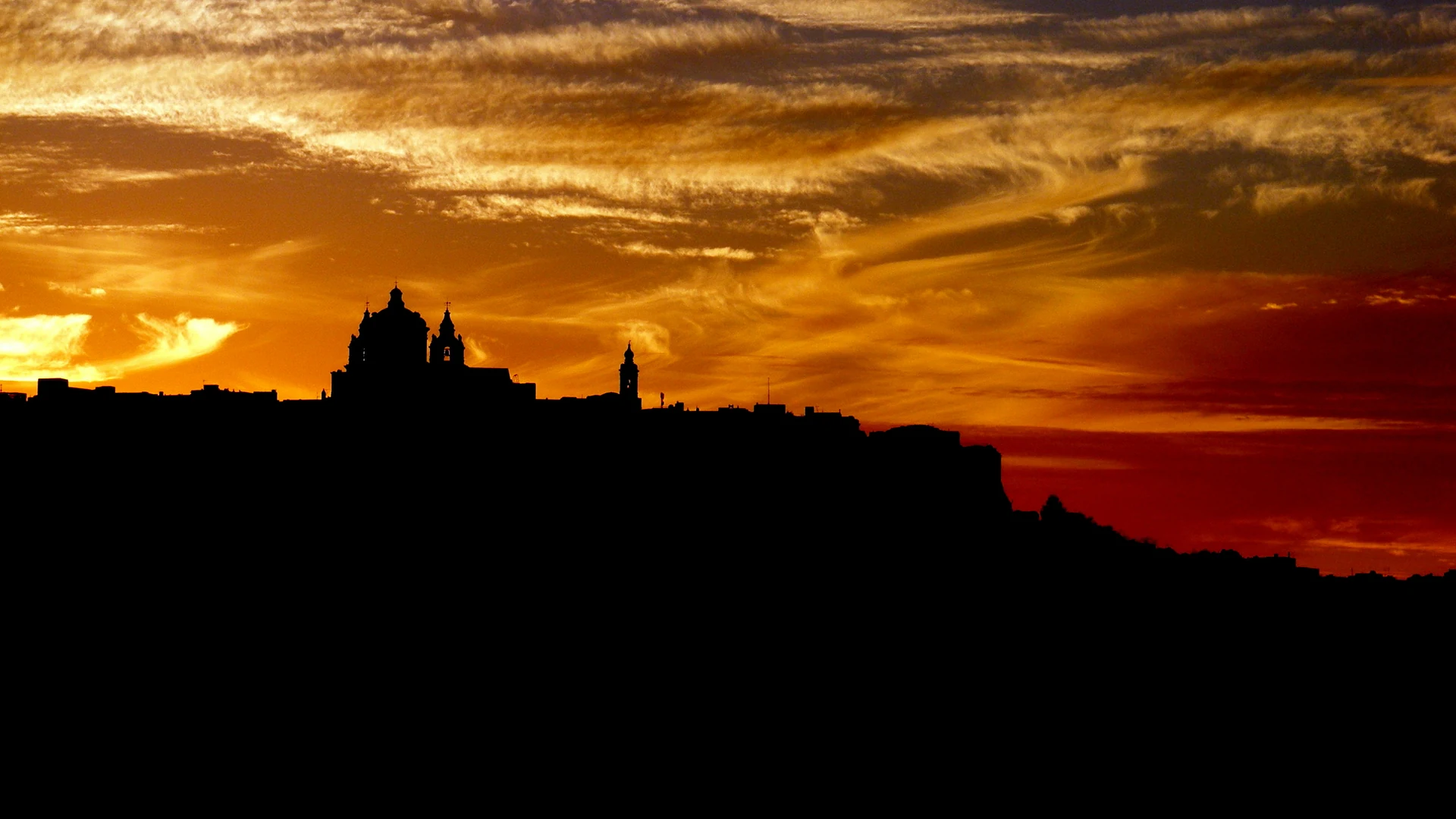 The skyline of Mdina, Malta's walled Silent City, silhouetted against a fiery sunset