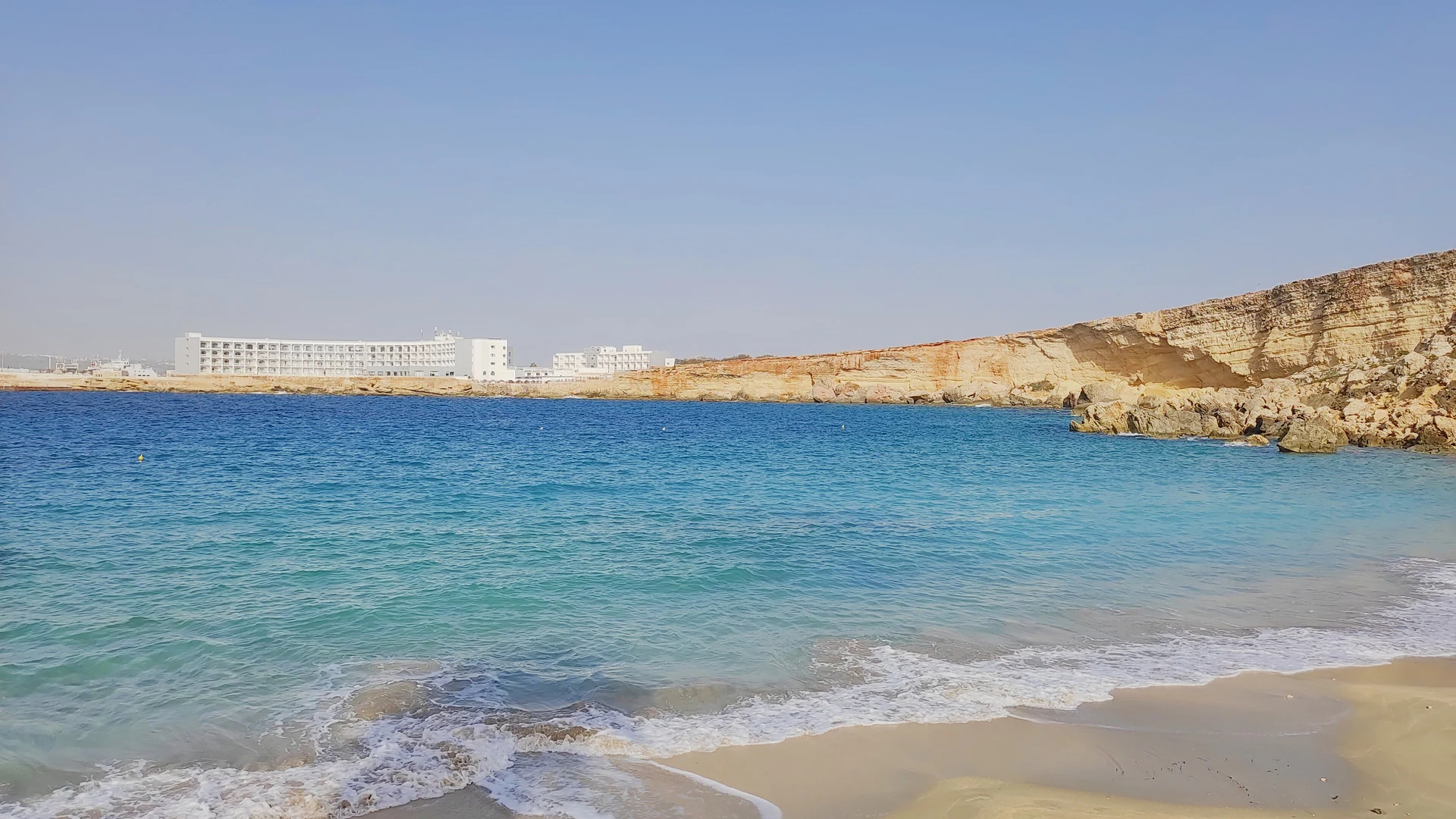 The turquoise water and sandy shore of Paradise Bay in northern Malta under a clear summer sky