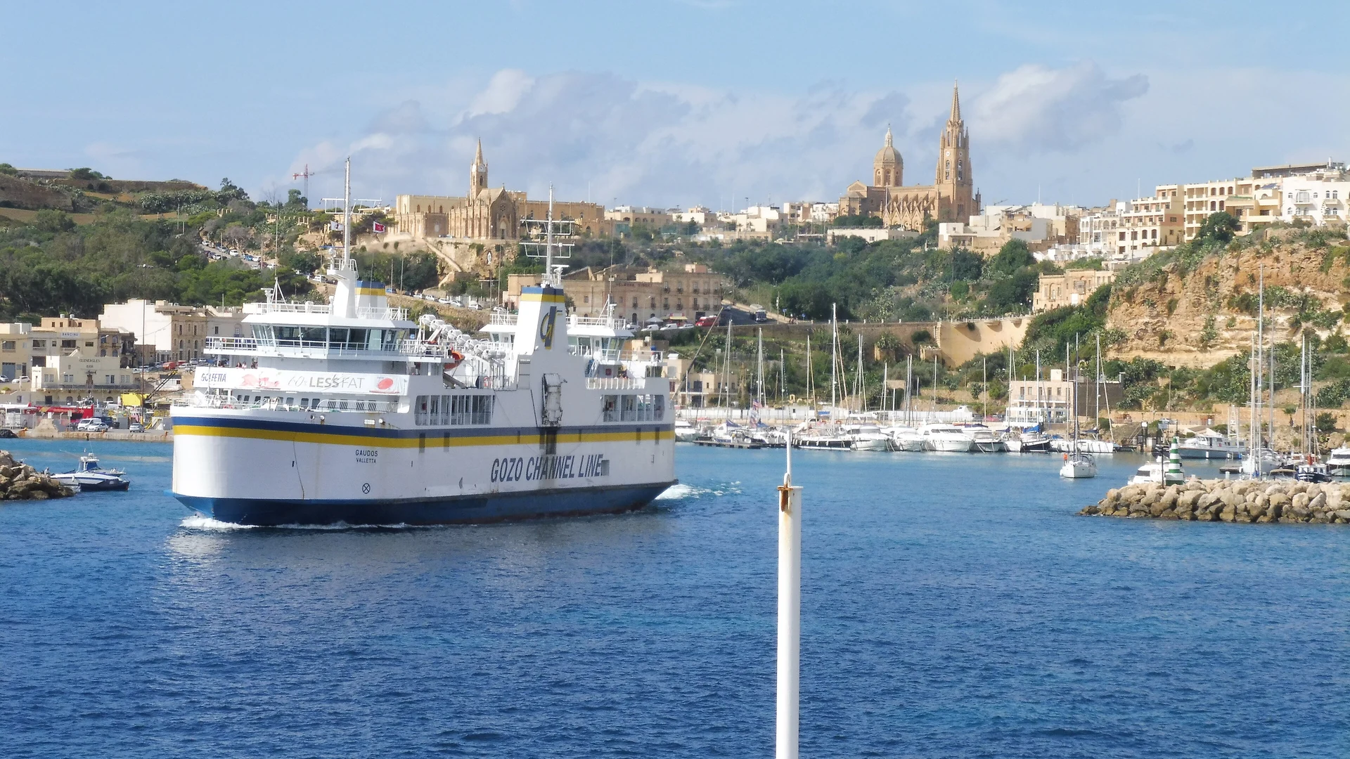 The Gozo Channel ferry Gaudos leaving Mġarr harbour, with the Għajnsielem churches on the hill behind